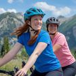 Zwei Radfahrerinnen lächeln während einer Fahrradtour in den Bergen, umgeben von üppigen Wäldern und klarer Bergluft.