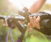 Nahaufnahme einer Hand mit Fahrradhandschuhen, die den Lenker hält, mit Sonnenlicht und unscharfem grünen Hintergrund.