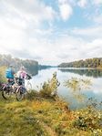 Zwei Radfahrer stehen am Ufer eines ruhigen Flusses und genießen die Aussicht auf das Wasser und die umgebenden Bäume.