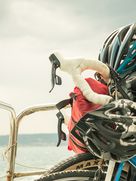 Nahaufnahme eines Fahrrads mit Helm und Packtaschen, das auf einer Fähre transportiert wird, mit Blick auf das Wasser und eine entfernte Küstenlinie.