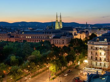 Abendstimmung in Wien mit Blick auf die beleuchtete Votivkirche, das Rathaus und die historische Ringstraße – eine beeindruckende Kulisse in der Dämmerung.