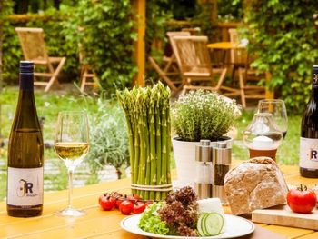 Ein gemütlich gedeckter Tisch in einem Gastgarten mit regionalen Spezialitäten, frischem Brot, Gemüse, Spargel und Weinflaschen – perfekt für eine genussvolle Pause nach einer Radtour.