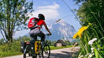Ein Radfahrer mit rotem Rucksack fährt auf einem Feldweg mit Blick auf einen majestätischen Berg und eine idyllische Landschaft.