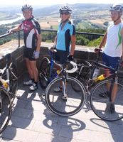 Drei Radfahrer stehen mit ihren Rennrädern an einem Aussichtspunkt mit Blick auf die Donau und die umliegende Landschaft.