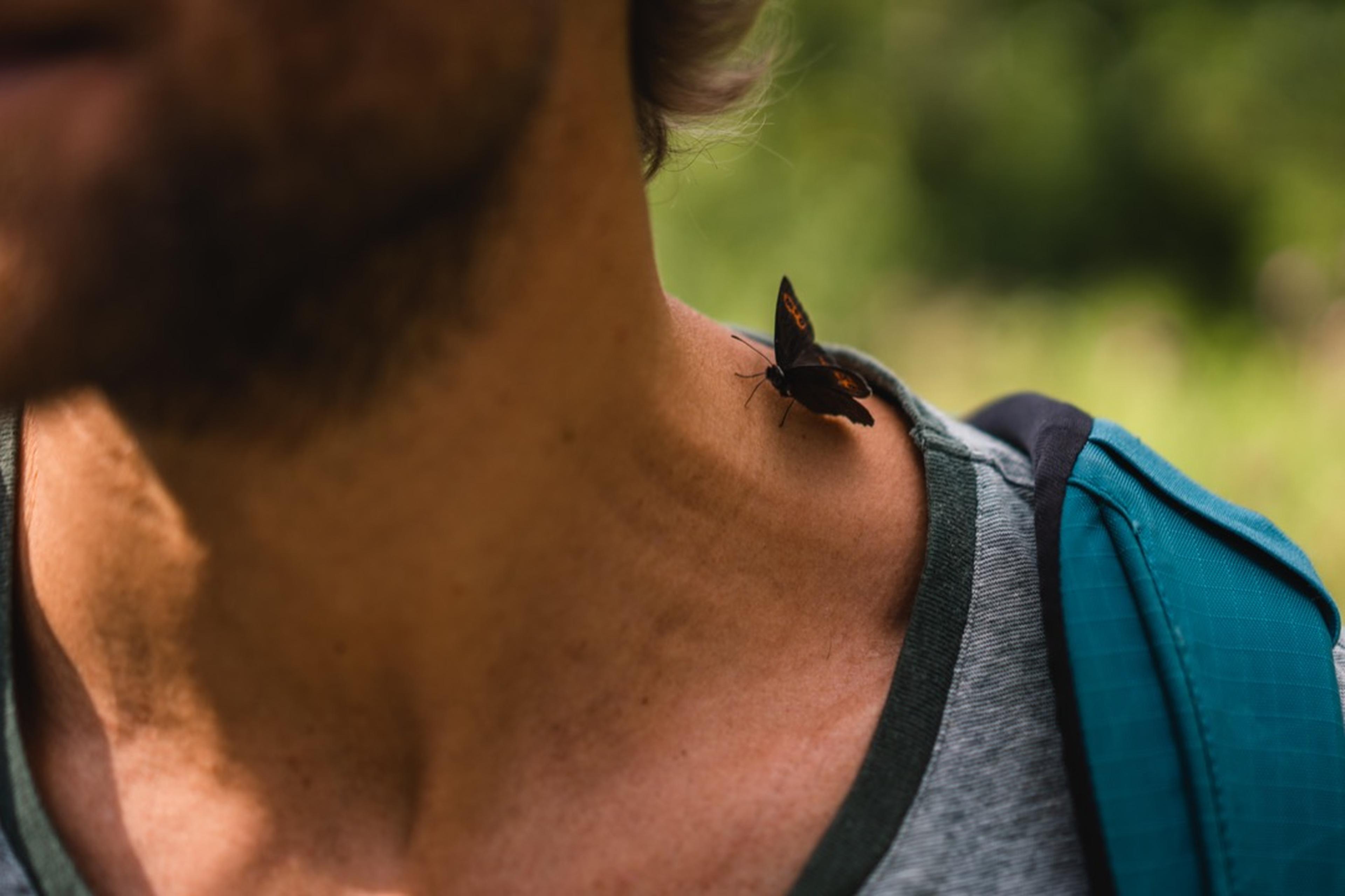 Ein Schmetterling sitzt auf dem Hals eines Mannes, dahinter Wald.