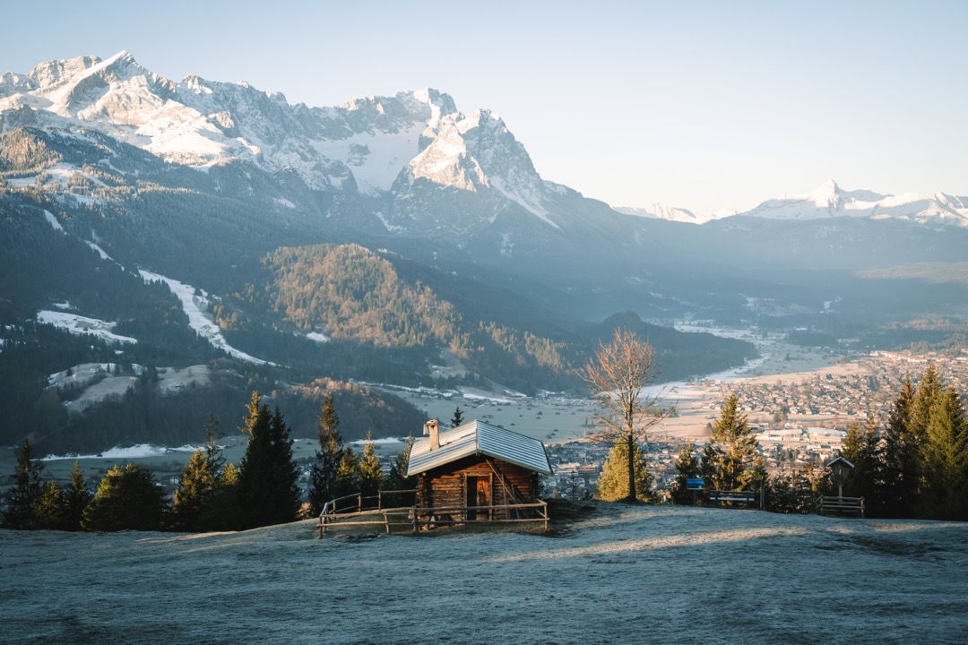 Bergpanorama mit Schnee, im Vordergrund eine kleine Holzhütte.