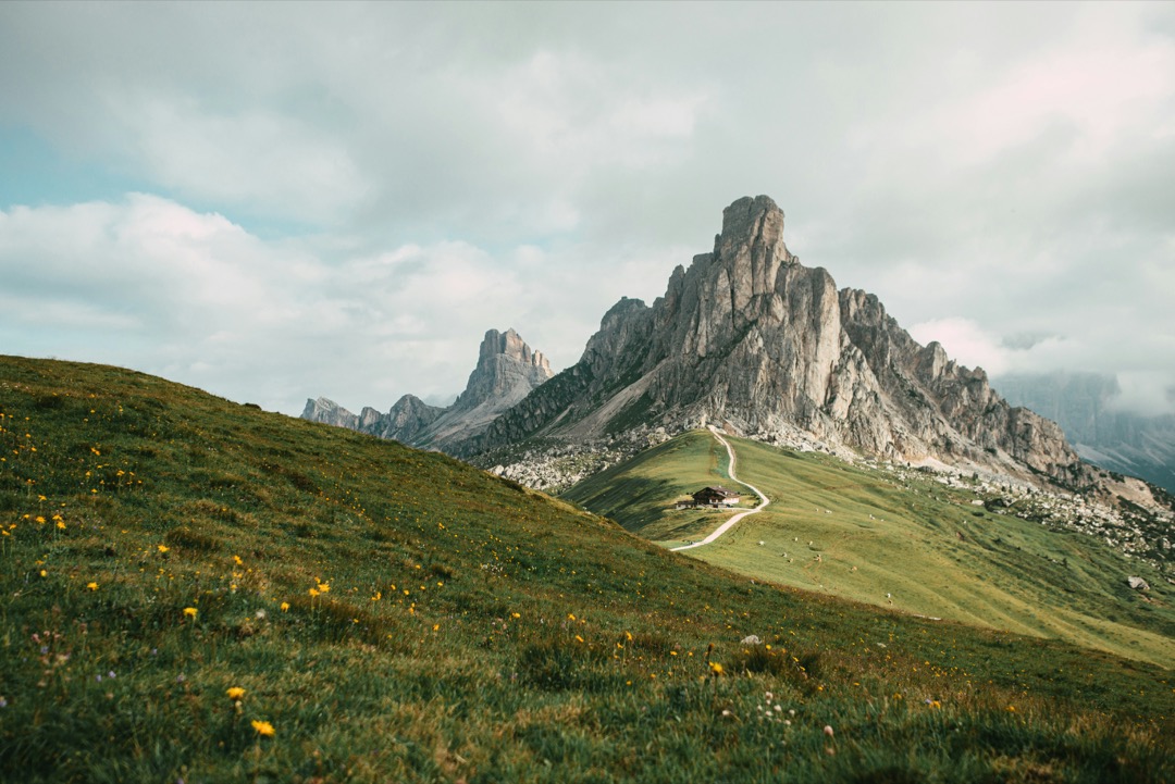 Ein Bergmassiv in Südtirol, ein Wanderweg auf grüner Wiese, eine Hütte in der Ferne.