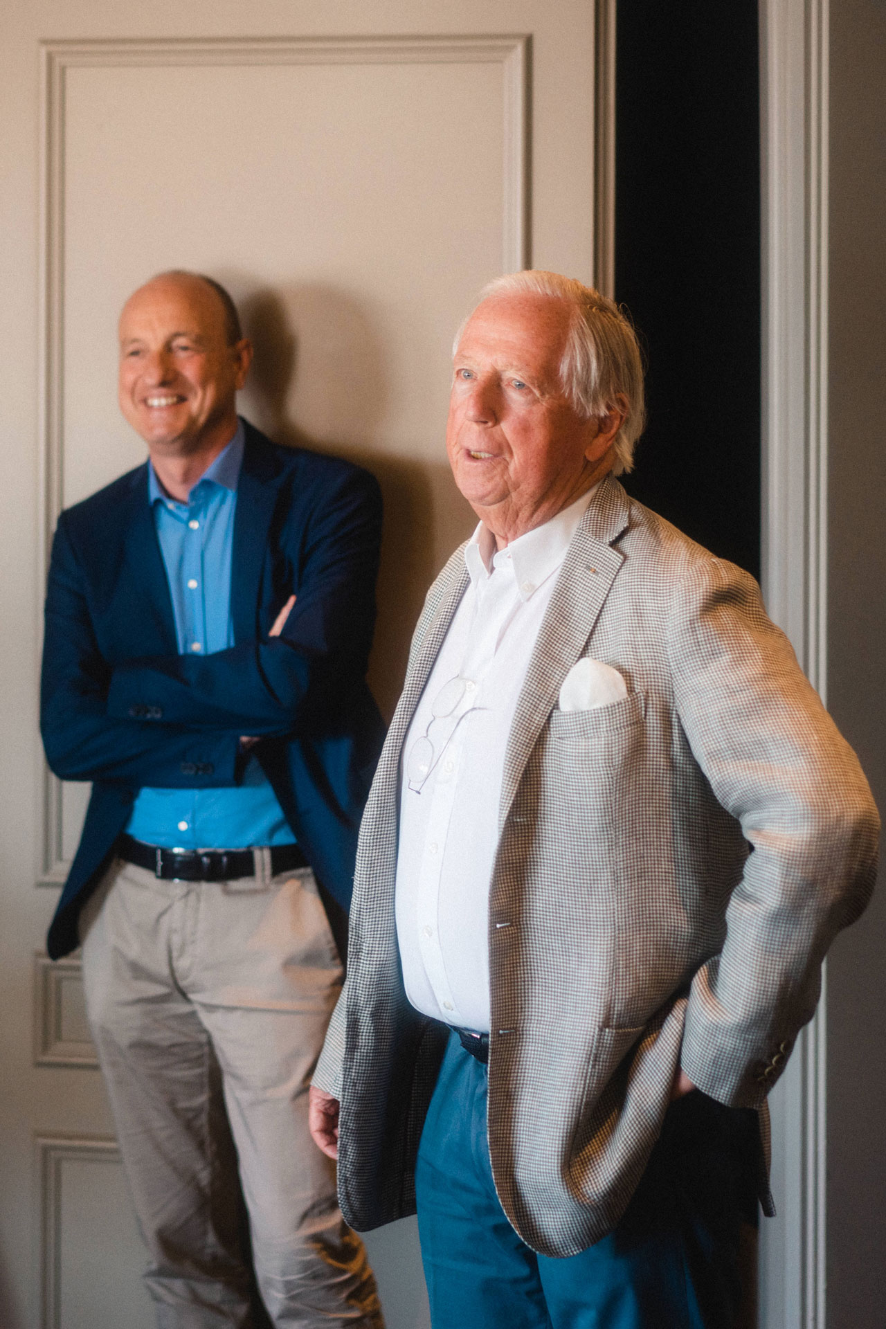 7fridays Gründer Horst Rahe in Hemd und Leinenanzug, daneben ein Mann in Anzug vor einer Zimmertür mit drei kunstvollen Kassetten.