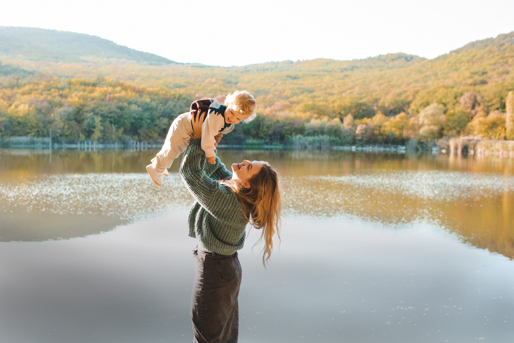 Frau mit Kind vor See, im Hintergrund herbstlicher Wald.