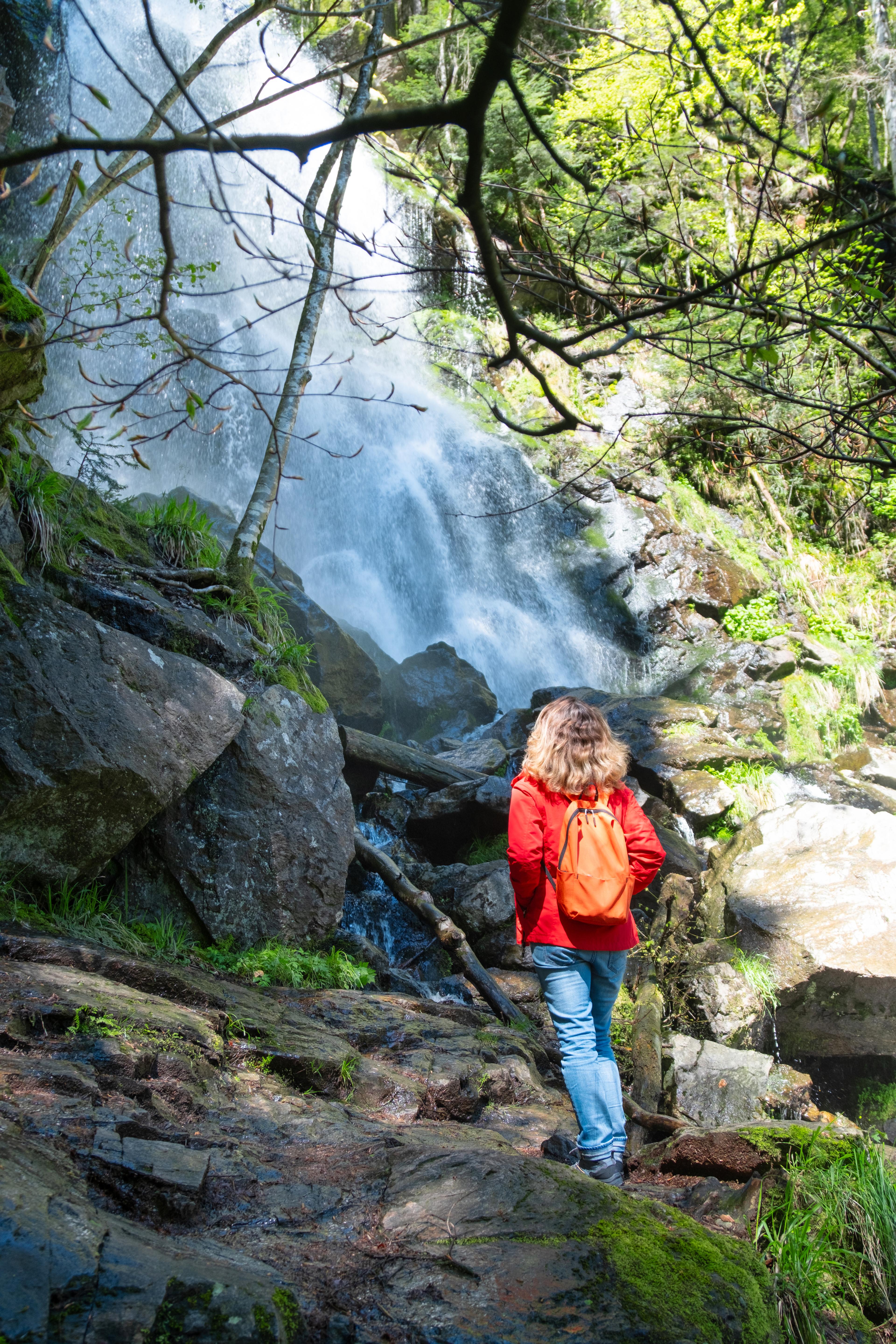 Eine Frau steht vor einem Wasserfall im Wald