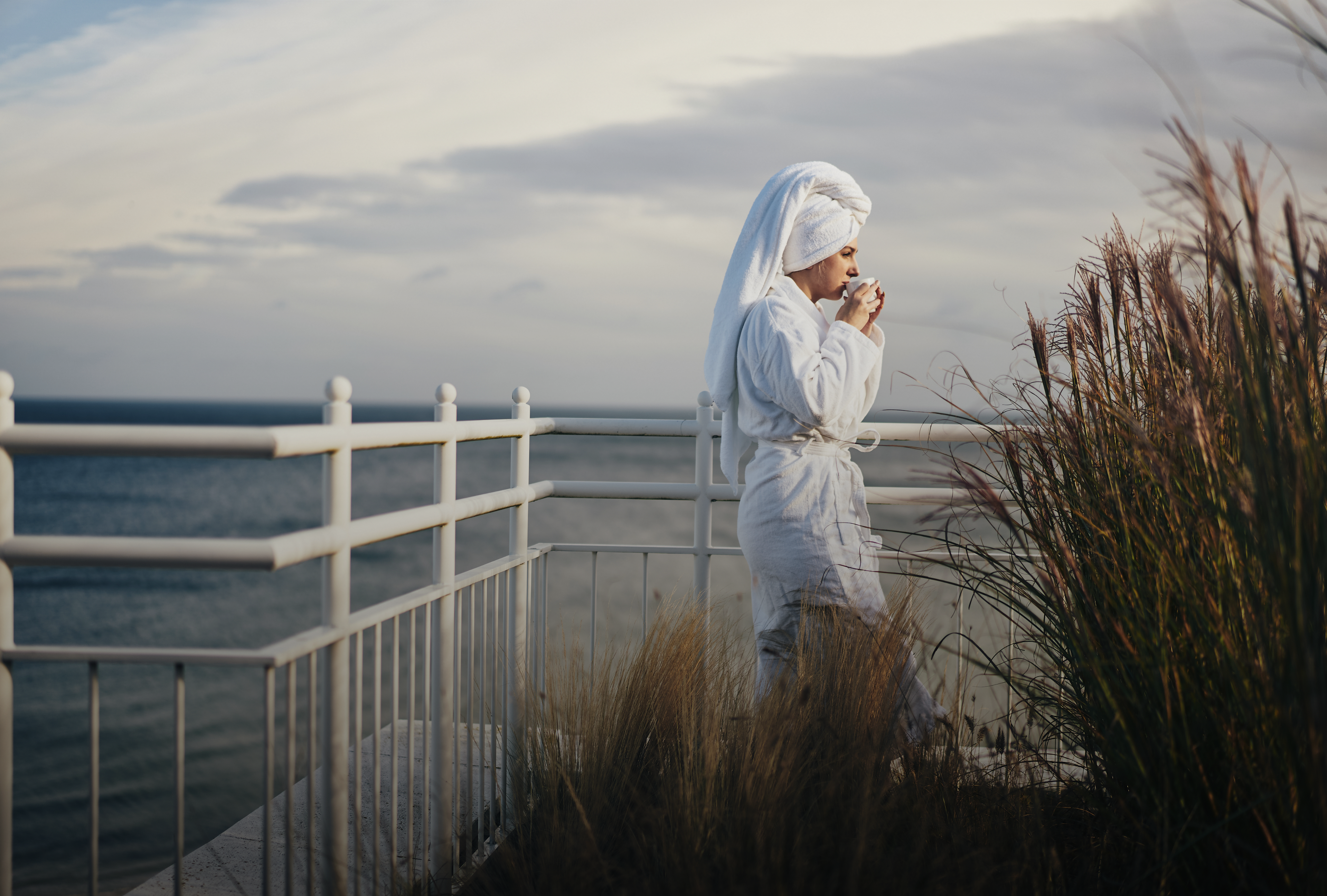 Frau steht mit Bademantel und Tasse am Meer