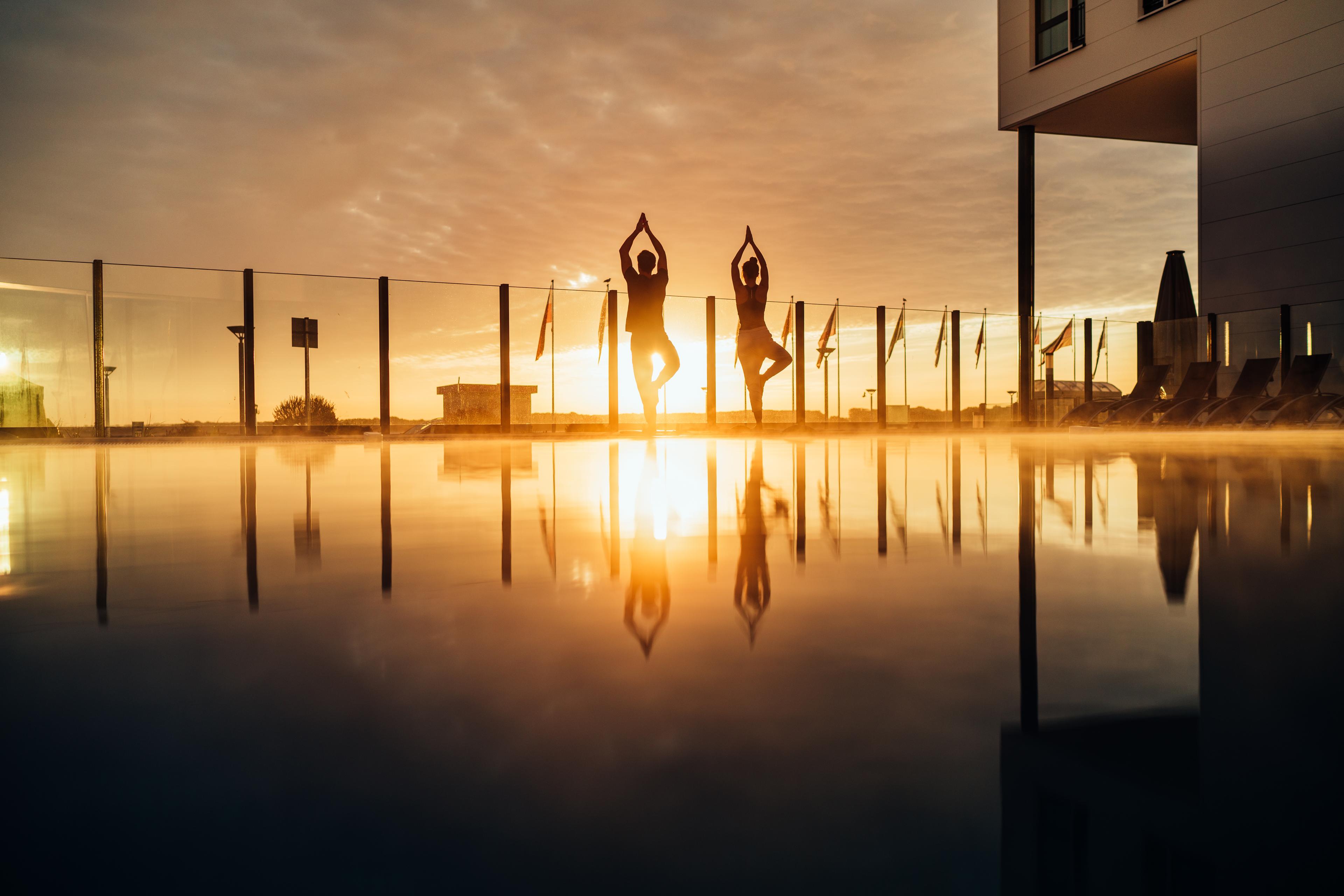 Zwei Menschen machen Yoga am Pool bei Sonnenuntergang