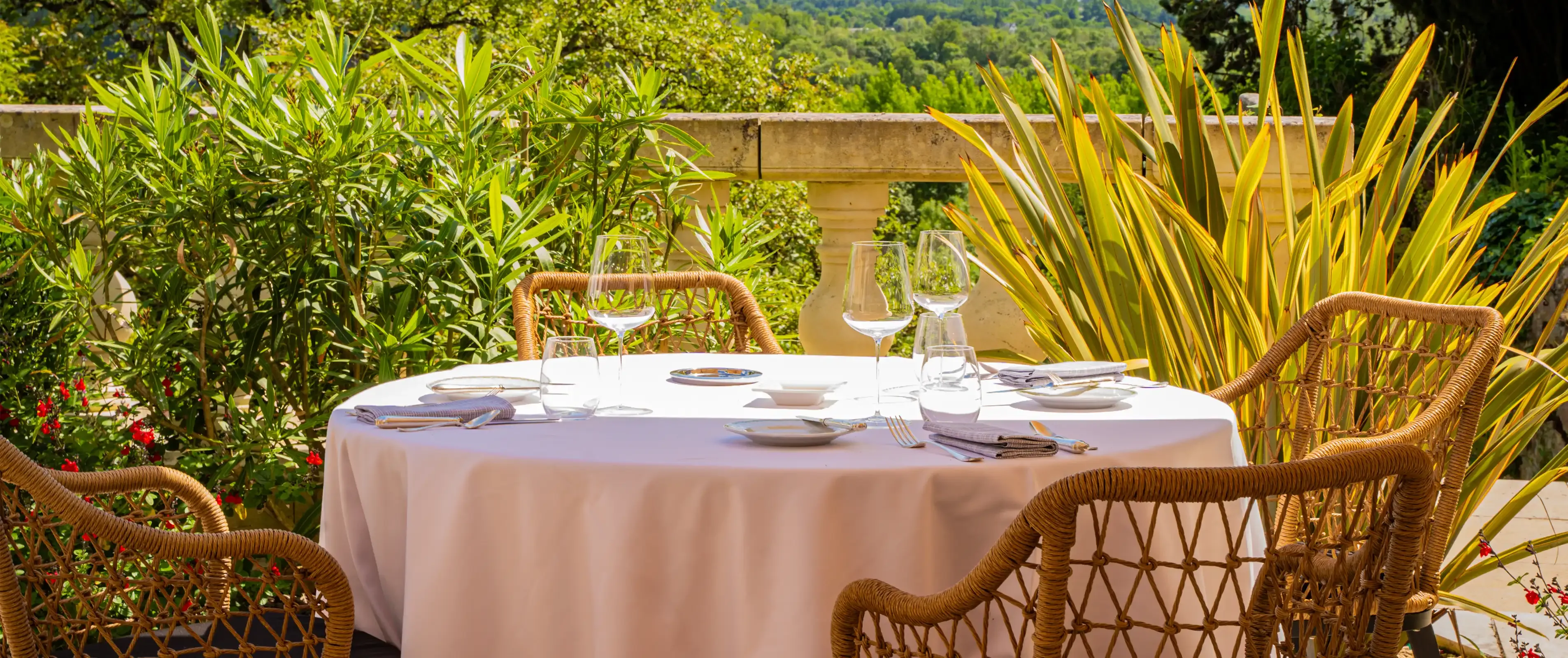 Table à manger, sur la terrasse du restaurant, recouverte d'une nappe blanche, dressée pour quatre personnes, entourée d'une végétation luxuriante et surplombant la vallée de la Loire sous un ciel partiellement nuageux.