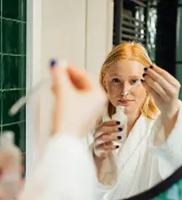 a woman holds a bottle of solution to a mirror