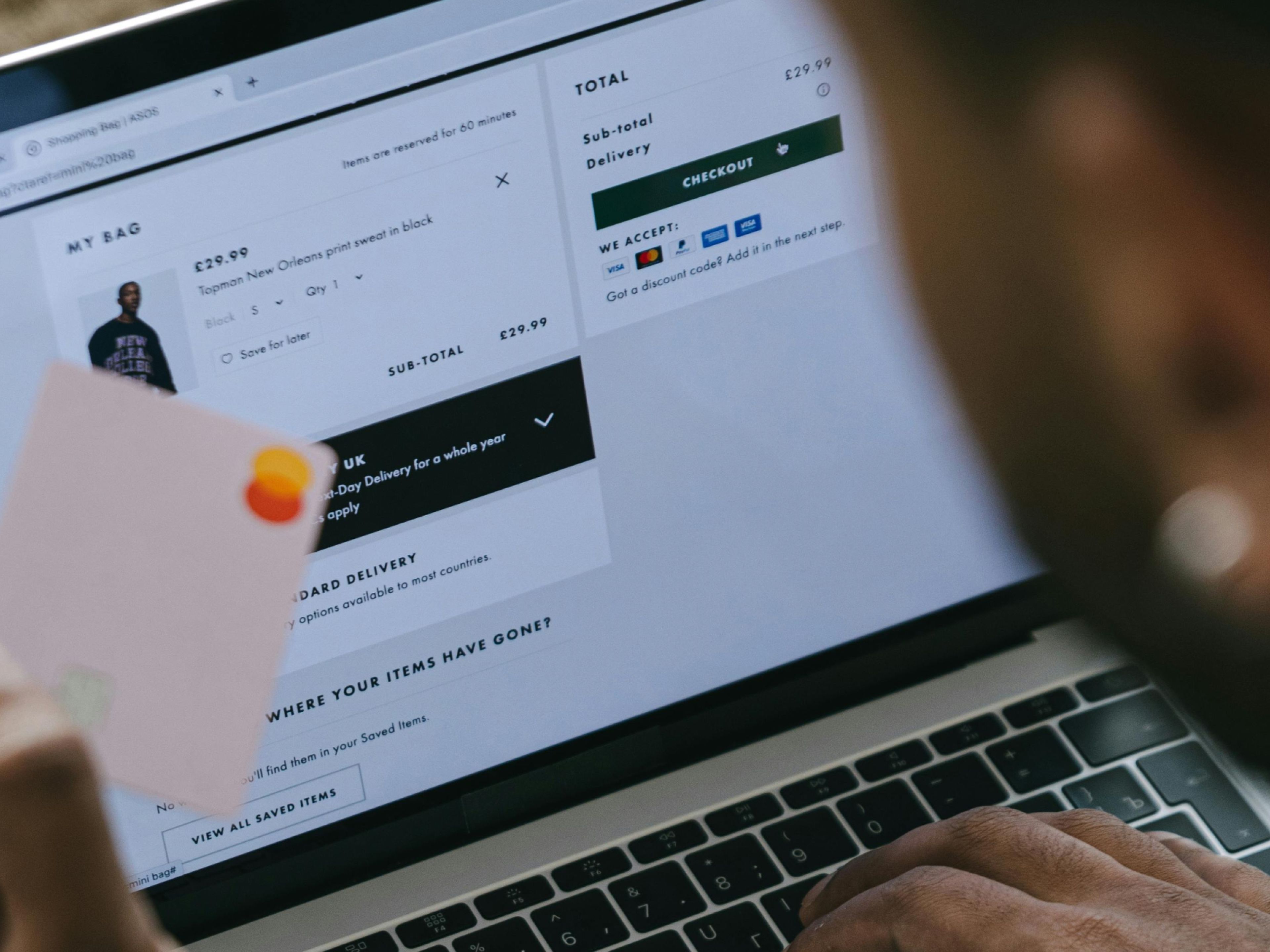 Photo showing a person holding a credit card, whilst looking at a website on a laptop computer