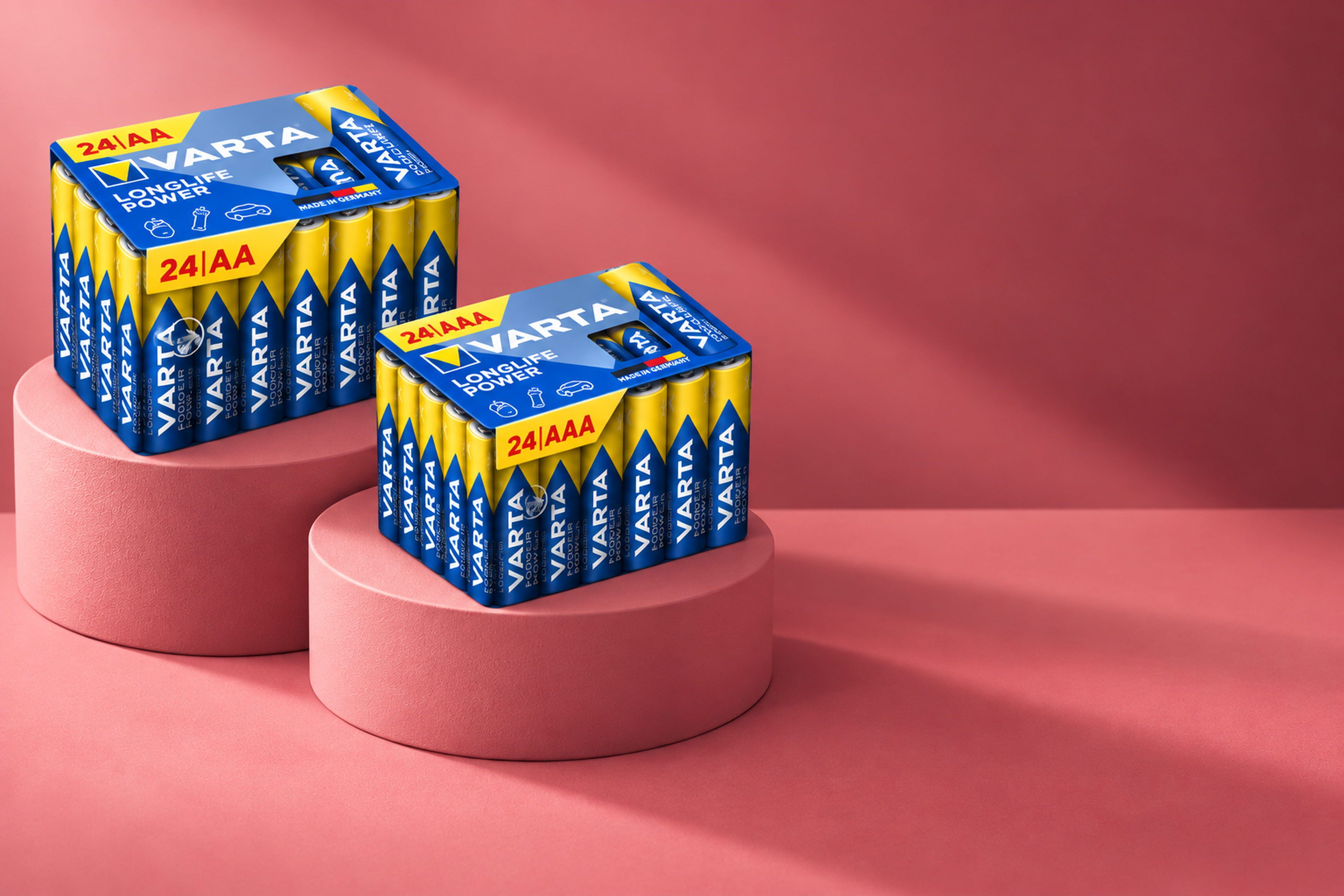 Two boxes of Varta batteries, 24 AA and 24 AAA, displayed on pink cylindrical platforms against a pink background.