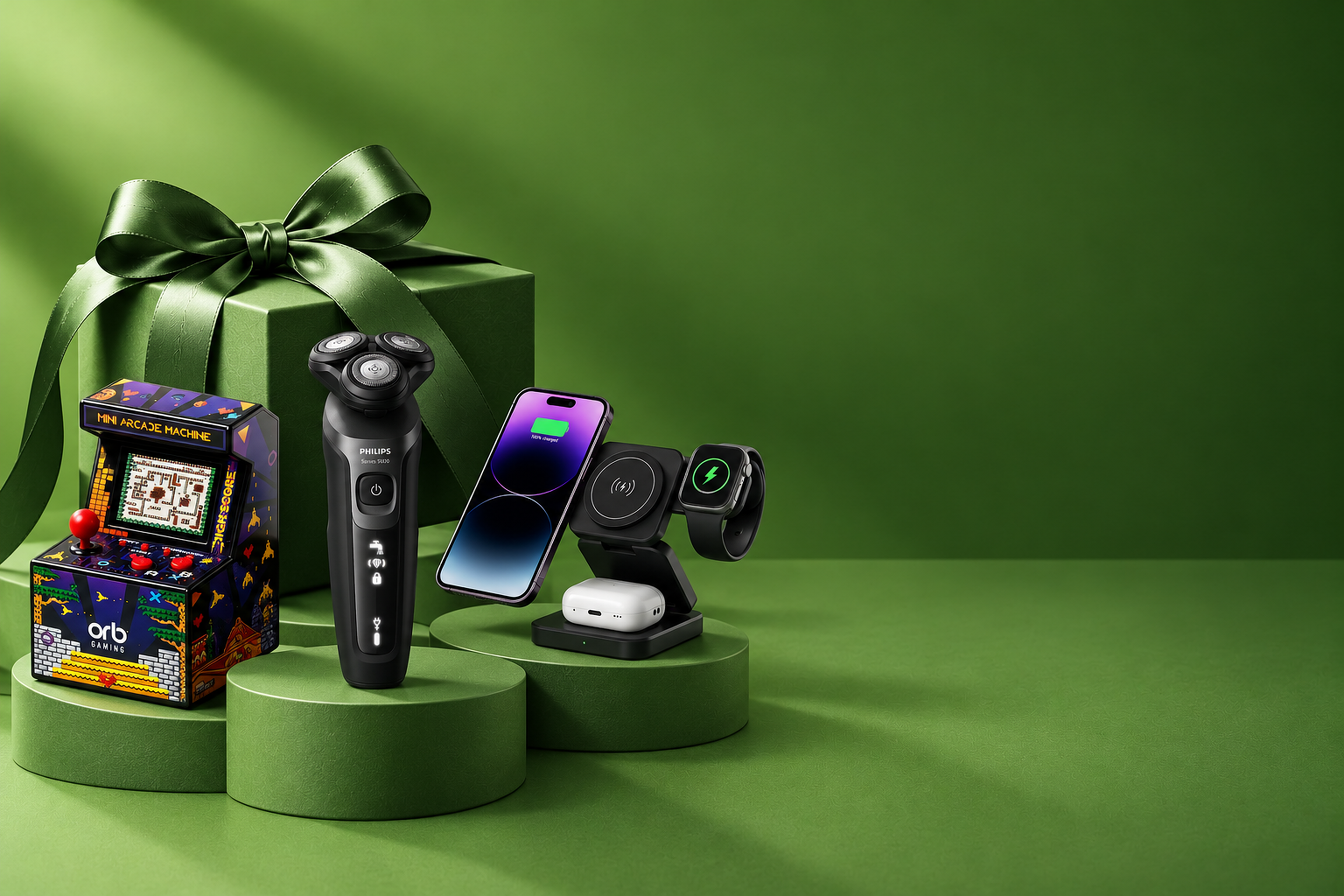 A festive arrangement of a green gift box with various gadgets, including a mini arcade, electric shaver, smartphone, wireless charger, and smartwatch.