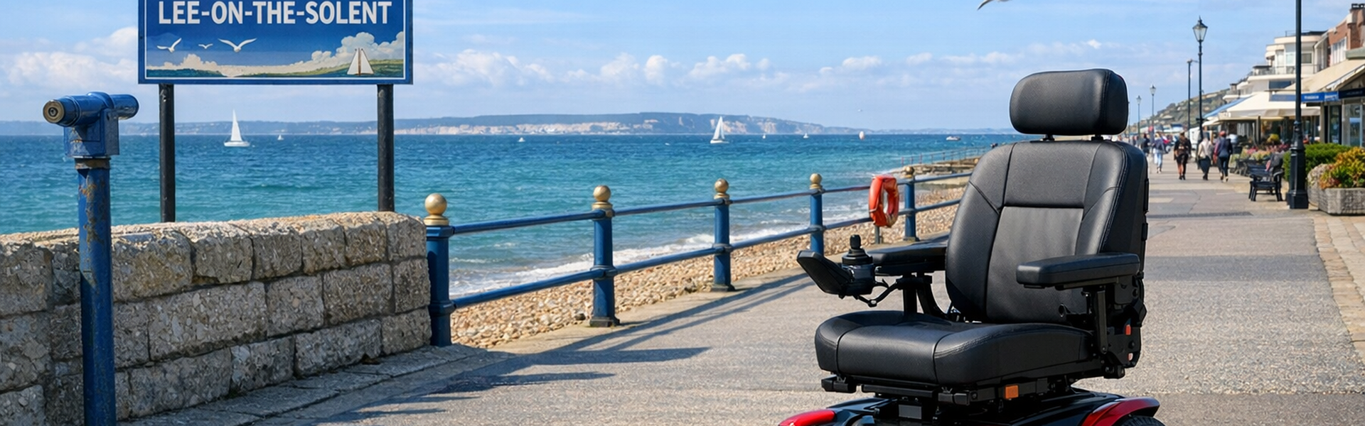 Electric wheelchair on a seaside promenade in Lee-on-the-Solent, with sailboats on the water and a clear blue sky above.