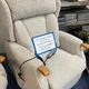 A beige recliner chair with a remote control and wooden armrests. A sign on the chair displays a sale price of £1,400, reduced from £1,800.