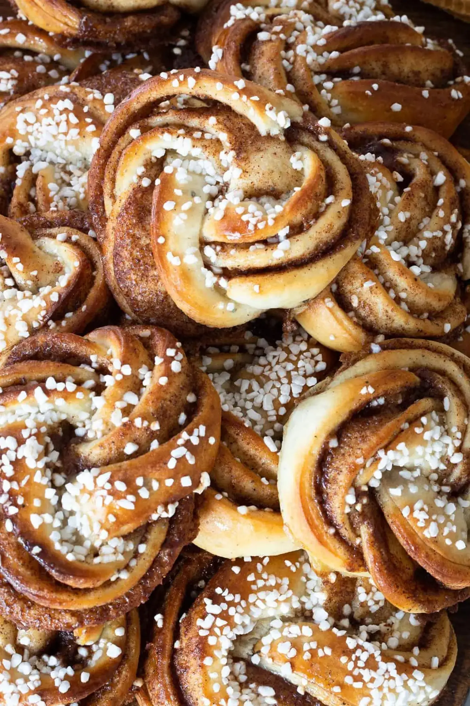 Close-up of cinnamon bun knots topped with coarse sugar, showcasing their golden-brown, twisted pastry and rich cinnamon filling.