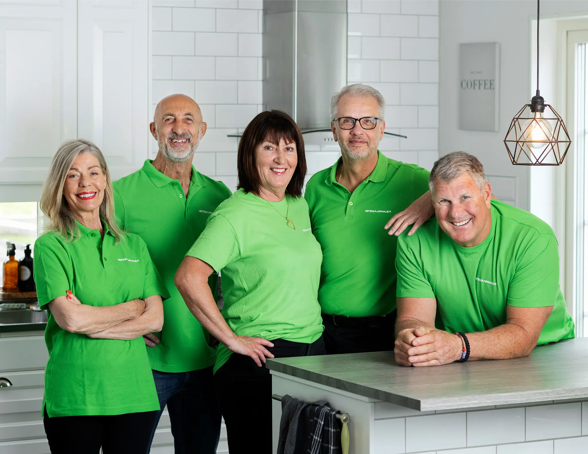 Fem jobbonärer står i ett kök och ler mot kameran