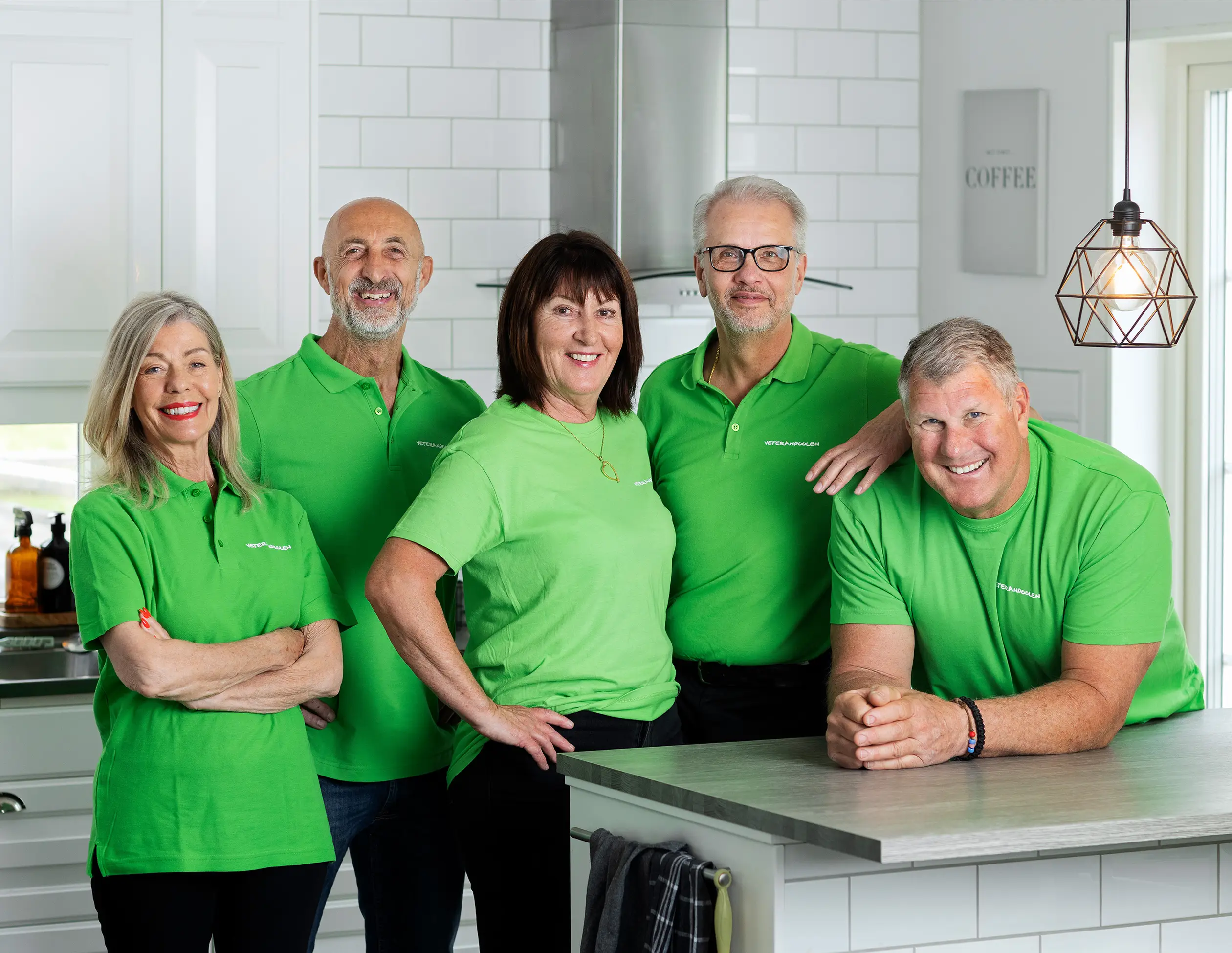 Fem jobbonärer står i ett kök och ler mot kameran