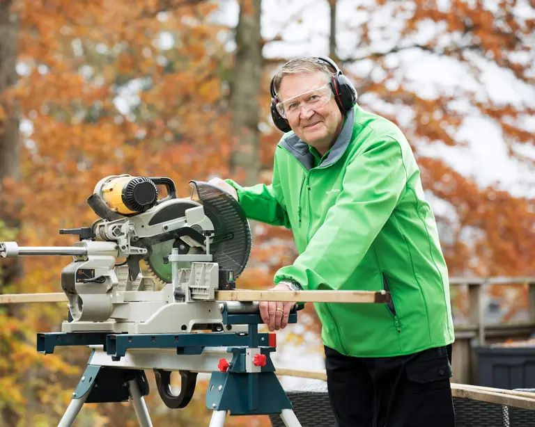 En man står och sågar med en cirkelsåg, han står utomhus och det är höstigt