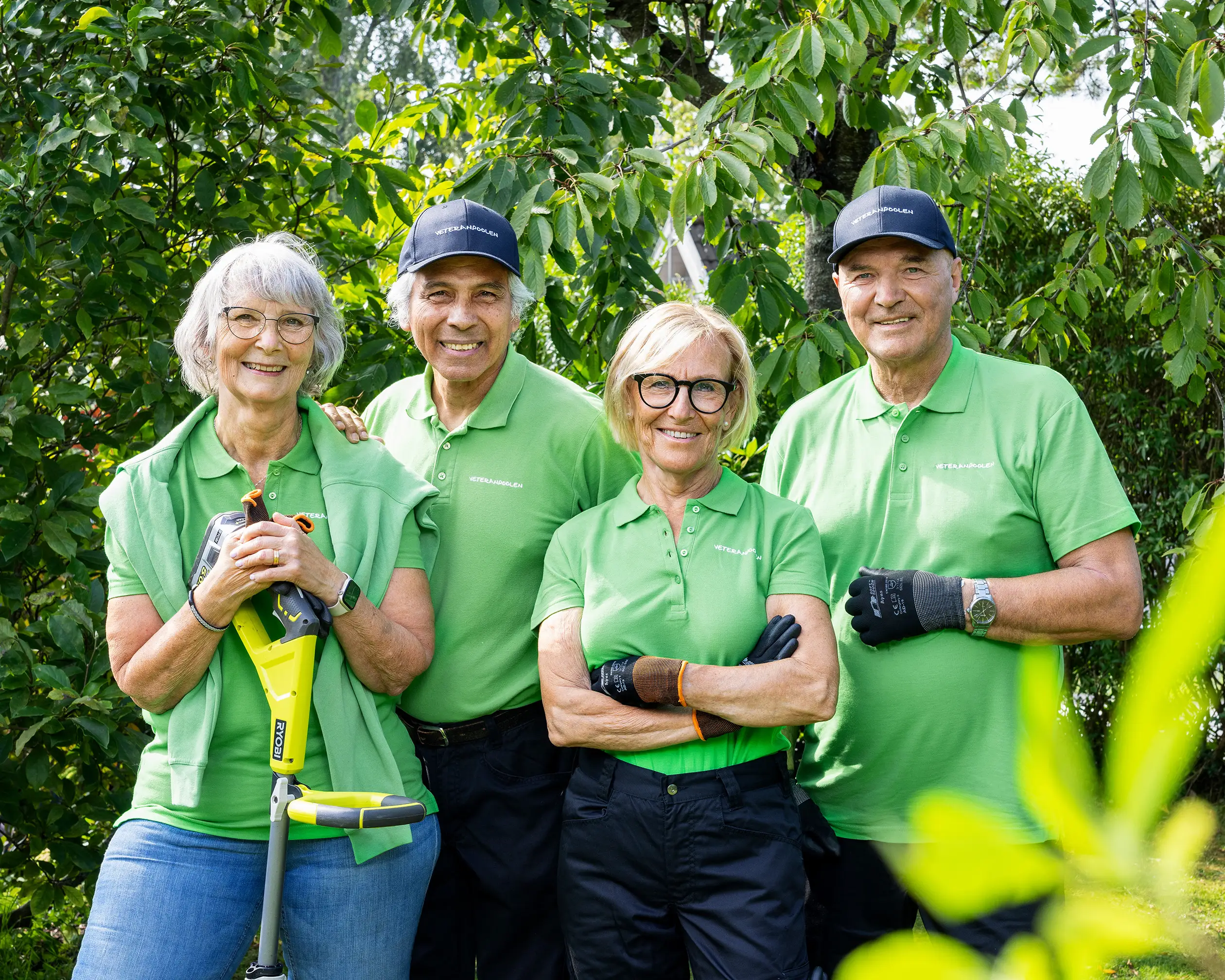 Fyra veteraner står bredvid varandra i en trädgård, de tittar mot kameran och ler