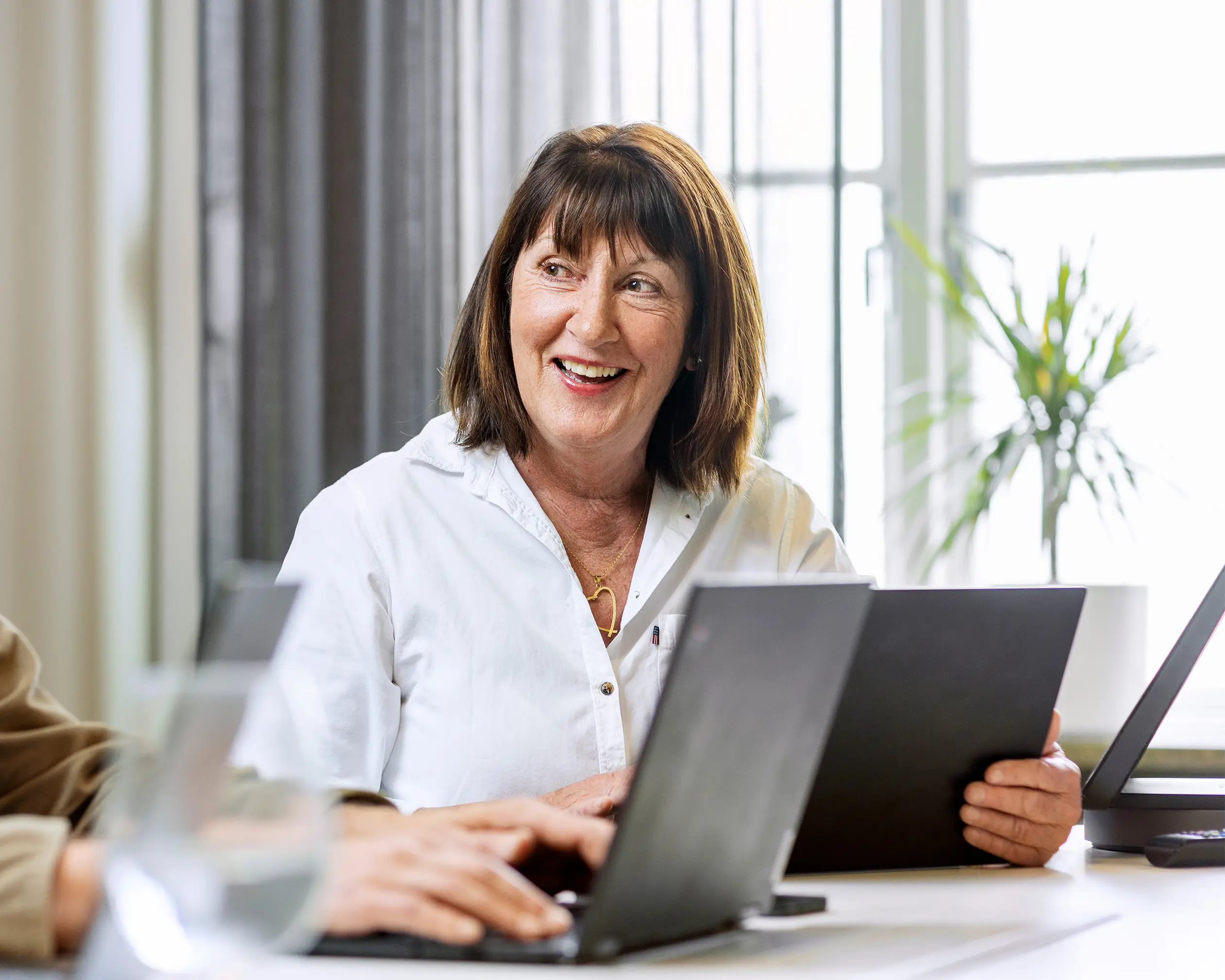 En kvinnlig veteran sitter på ett kontor med en laptop fram för sig, hon tittar mot en kollega och ler