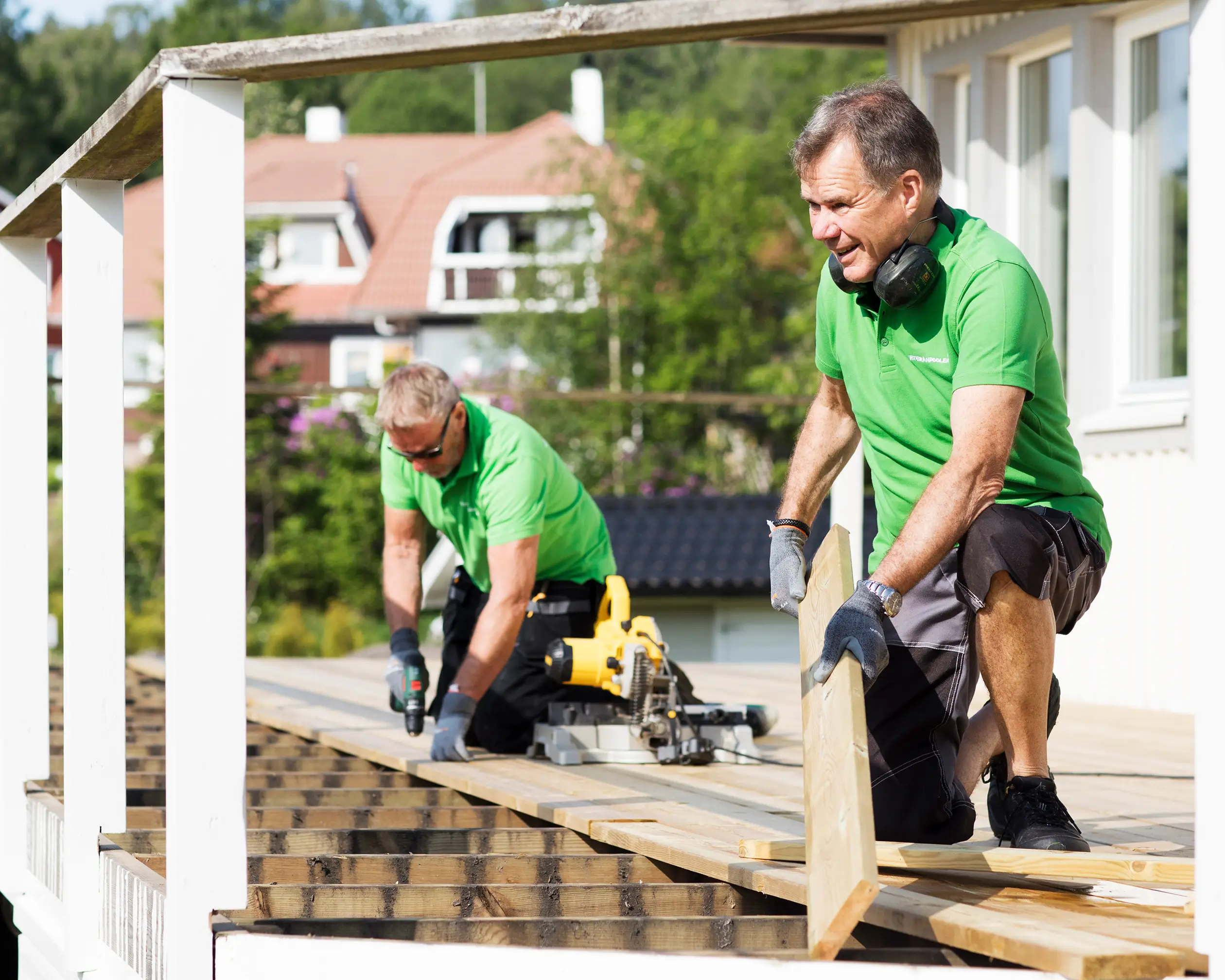 Två snickare arbetar på en altan, det är soligt väder och de ser nöjda ut