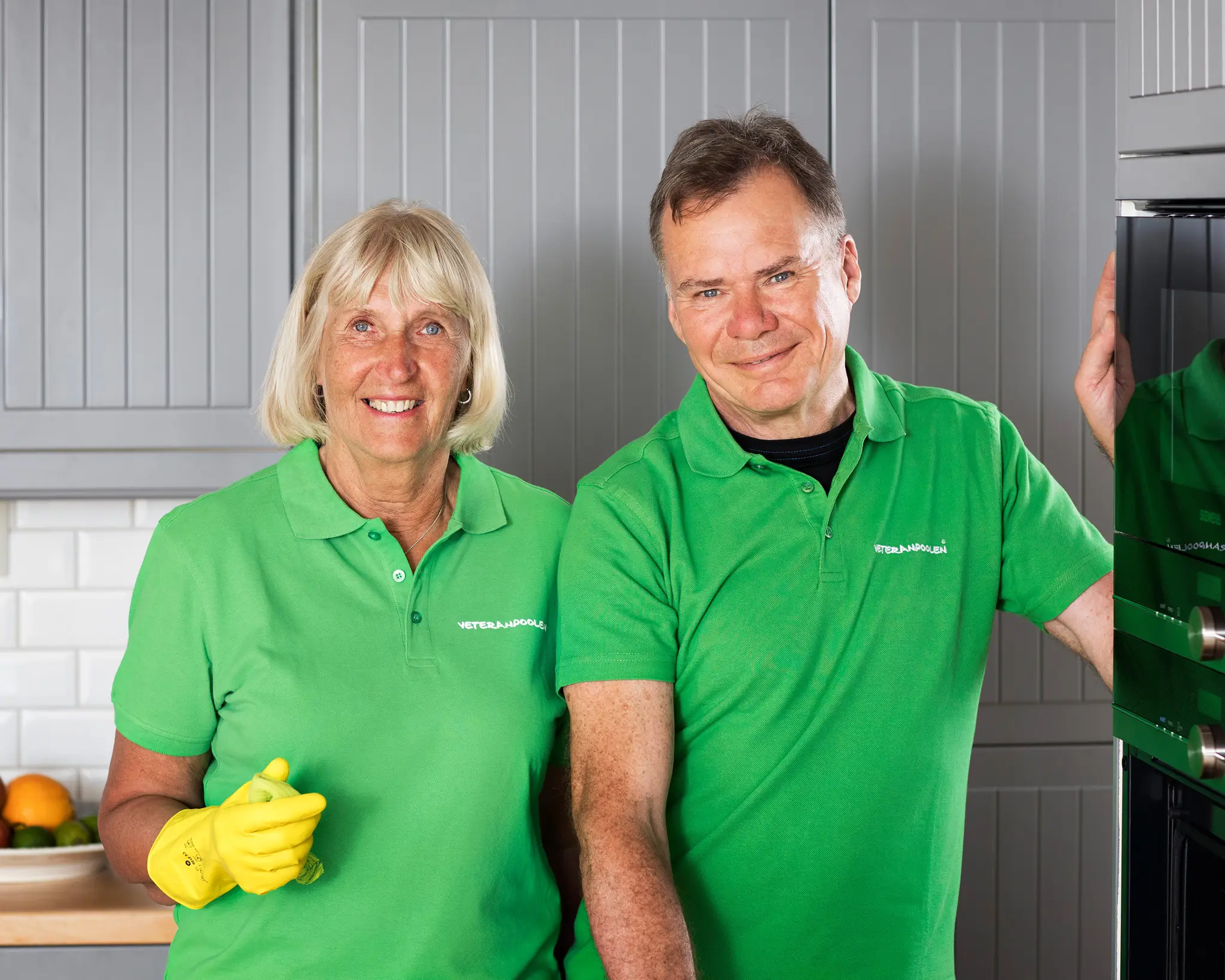 En kvinnlig och en manlig jobbonär står i ett kök bredvid varandra, de har gula gummihandskar och ska städa.