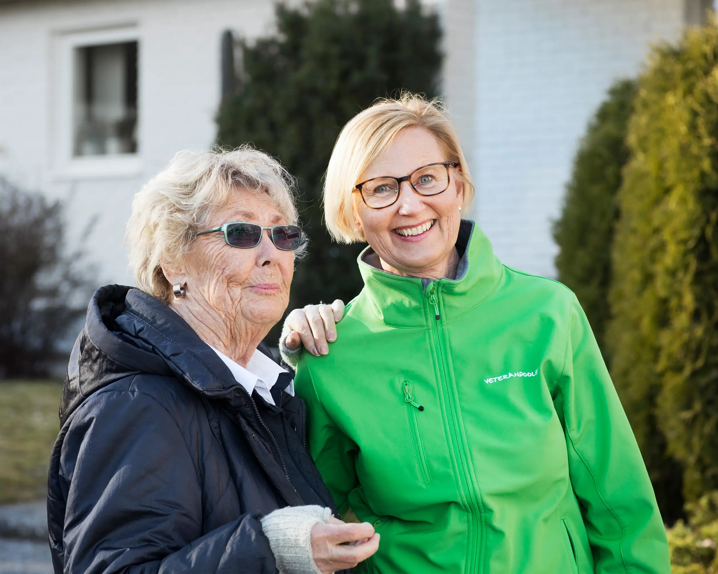 Två äldre kvinnor i går en promenad, det ser höstigt ut. Den ena kvinnan har en grön jacka och tittar mot kameran och ler.