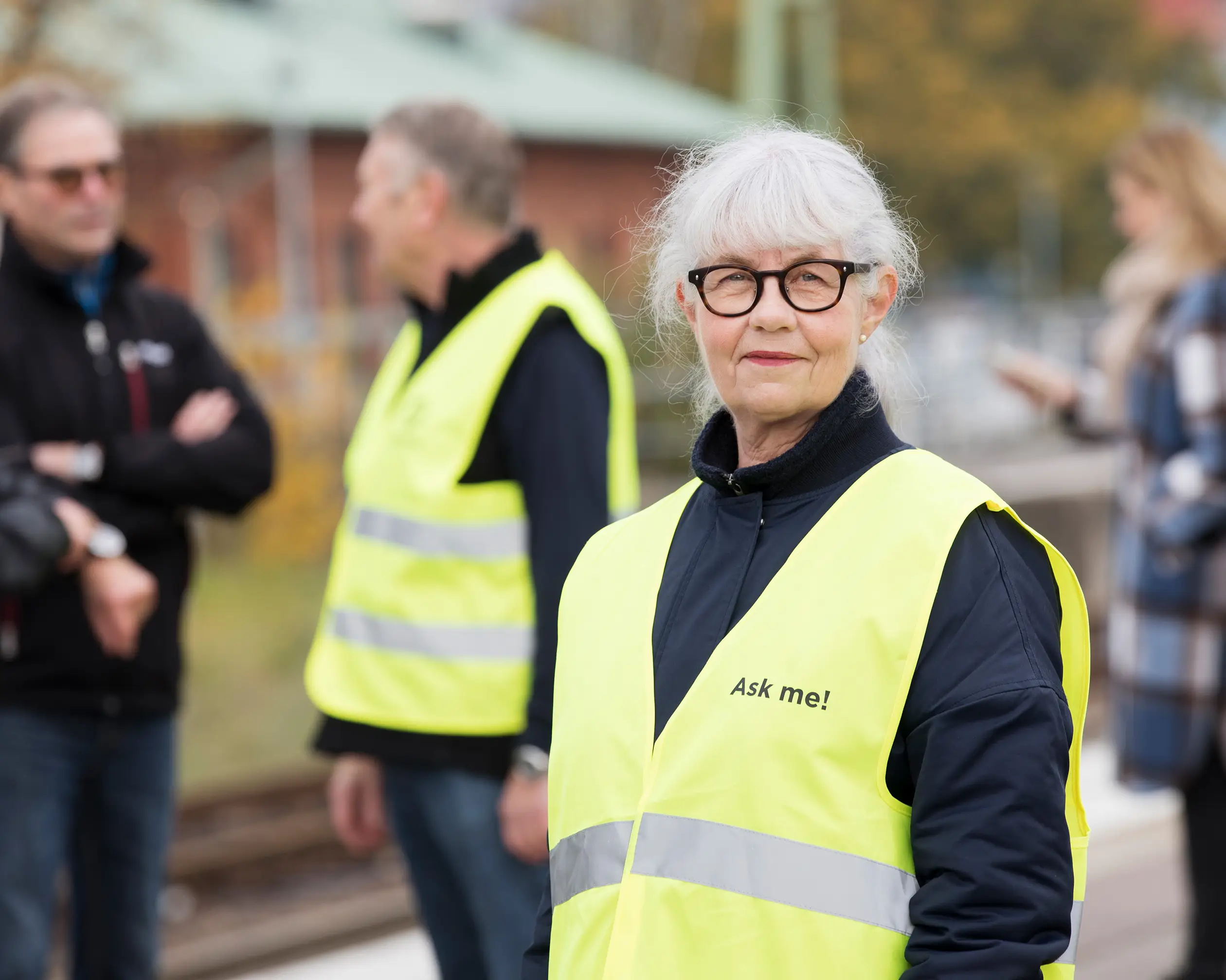 Kvinnlig jobbonär har en reflexväst på sig, ler och tittar mot kameran, hon står på en tågperrong.
