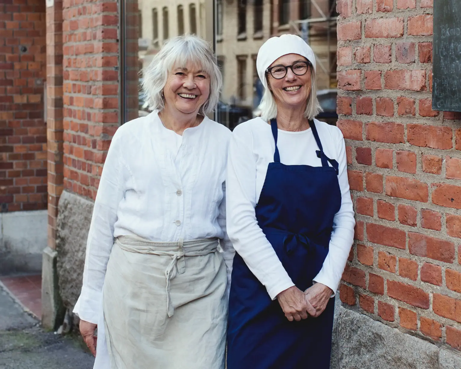 Två jobbonärer i serveringskläder står utanför en tegelbyggnad