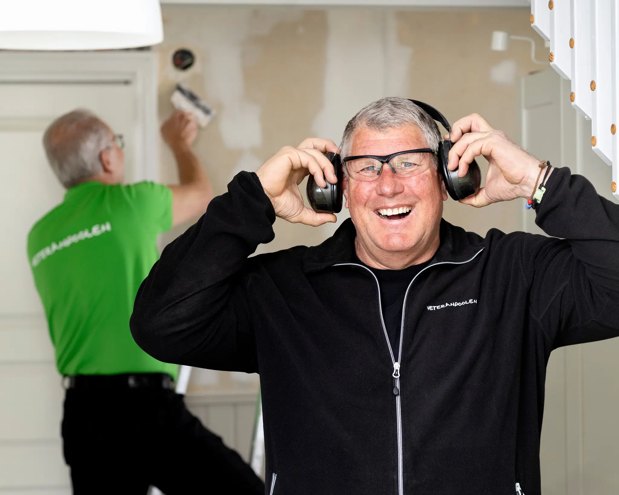 En man med hörlurar ler mot kameran, han lyfter på hörlurarna och ser glad ut