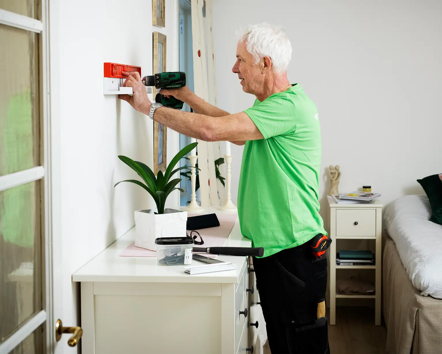 En manlig pensionär sätter upp en hylla, han har ett vattenpass och skruvdragare