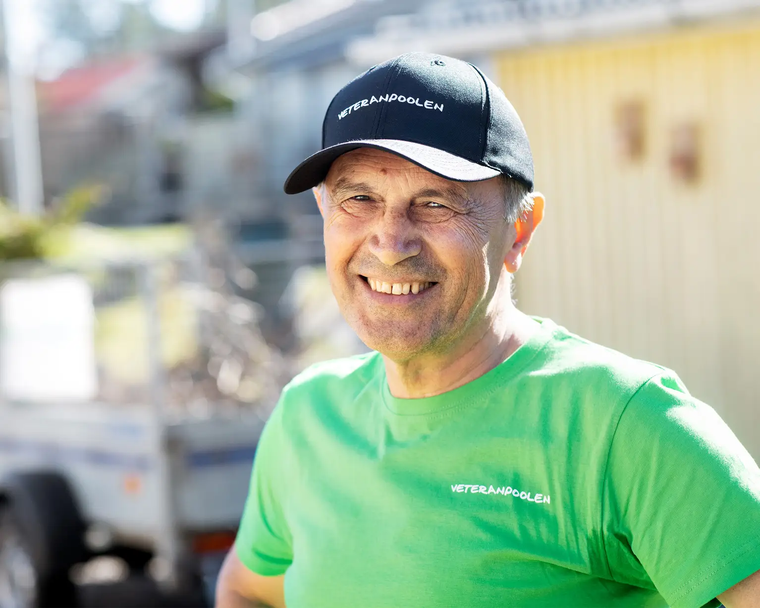 En man med grön tröja och svart keps ler mot kameran