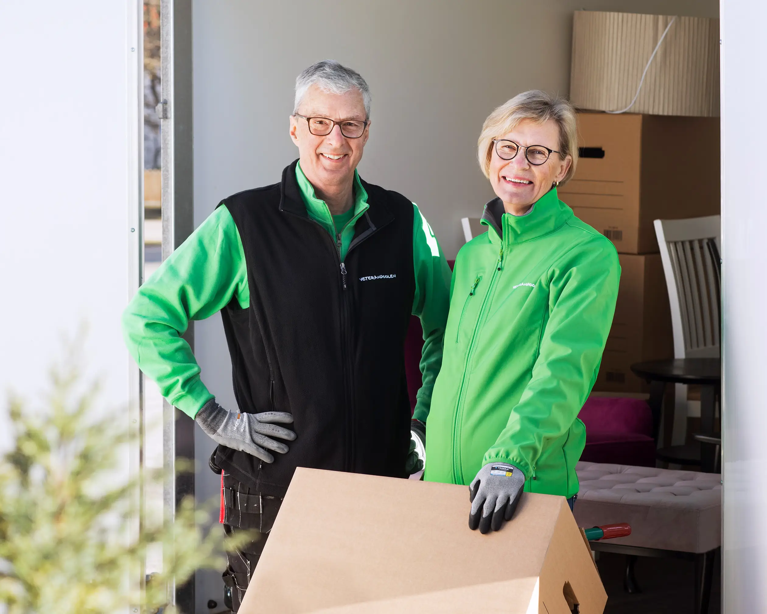 Två veteraner står vid en skåpbil fylld med flyttlådor, de tittar mot kameran och ler