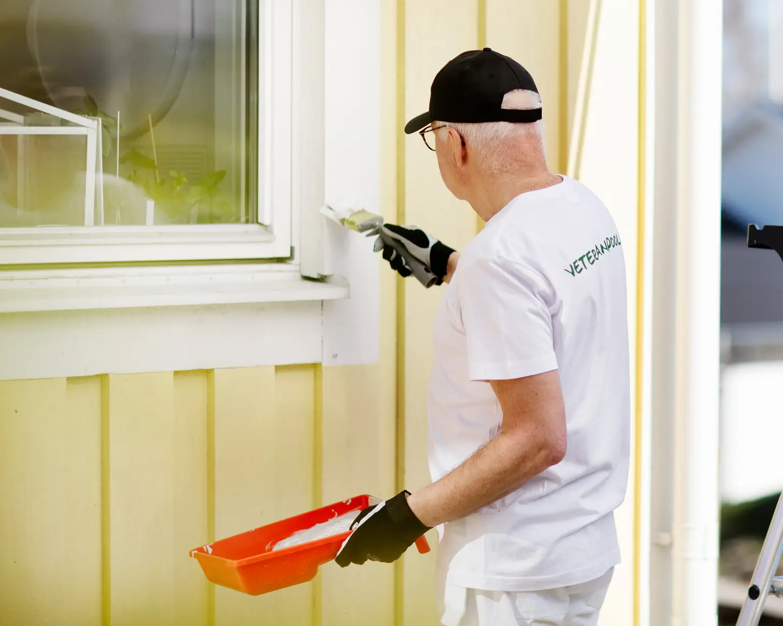 En man står med pensel och målar listerna runt ett fönster utomhus