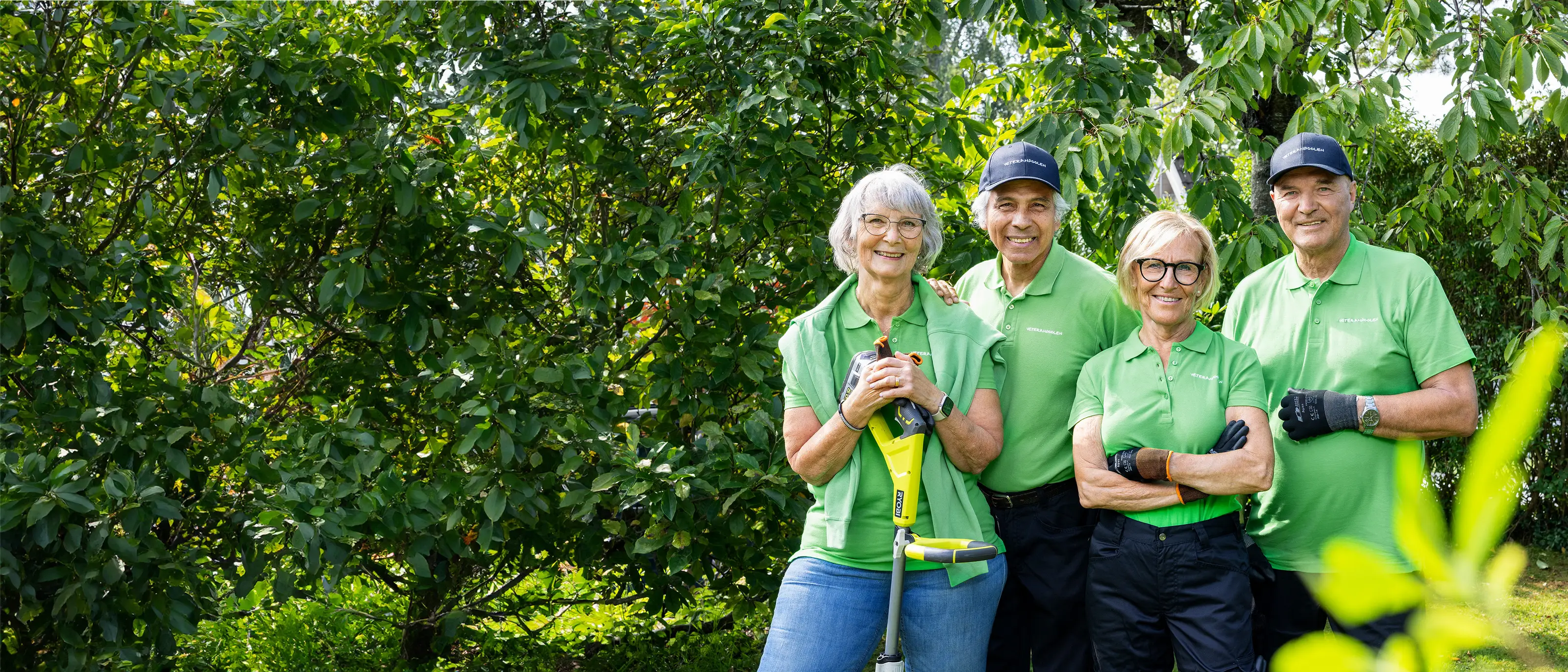 Grupp trädgårdsjobbonärer står i gröna t-shirts och ler mot kameran
