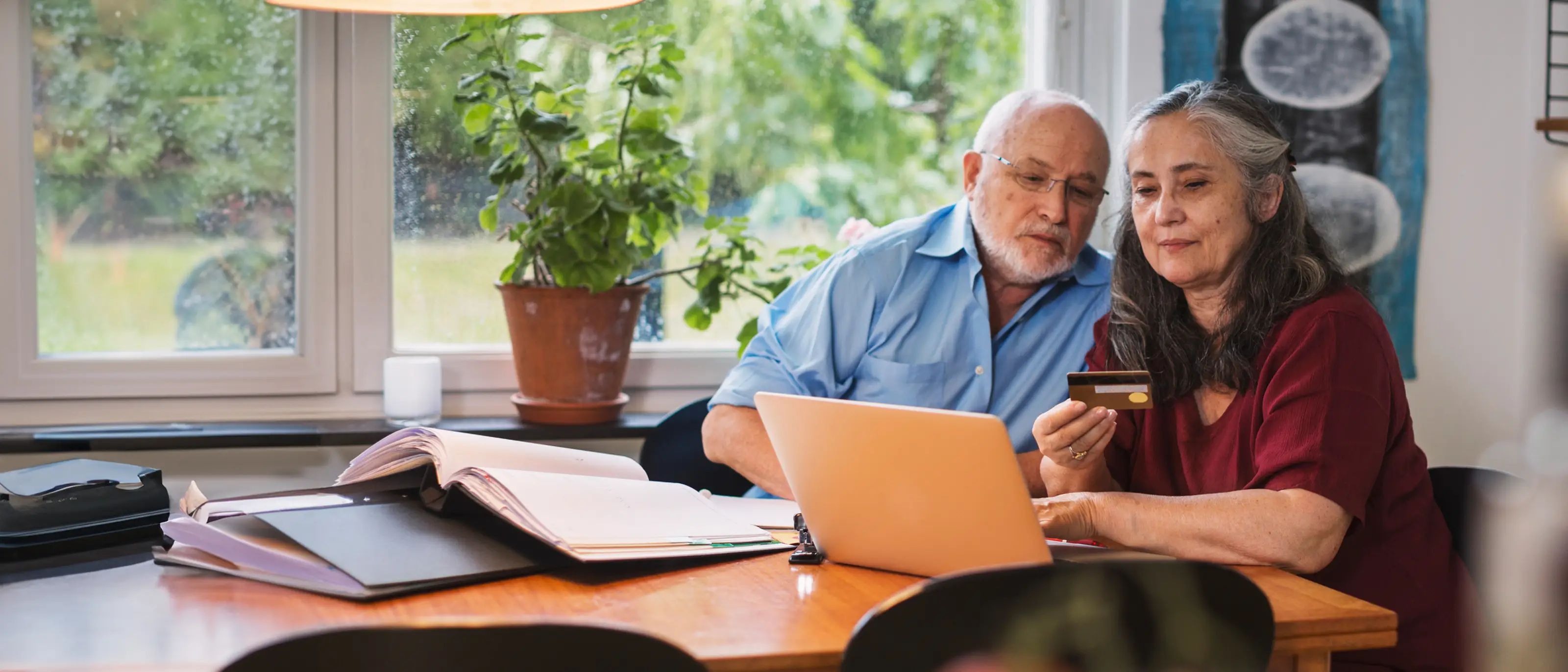Två pensionärer sitter i ett kök och kollar på ett kreditkort