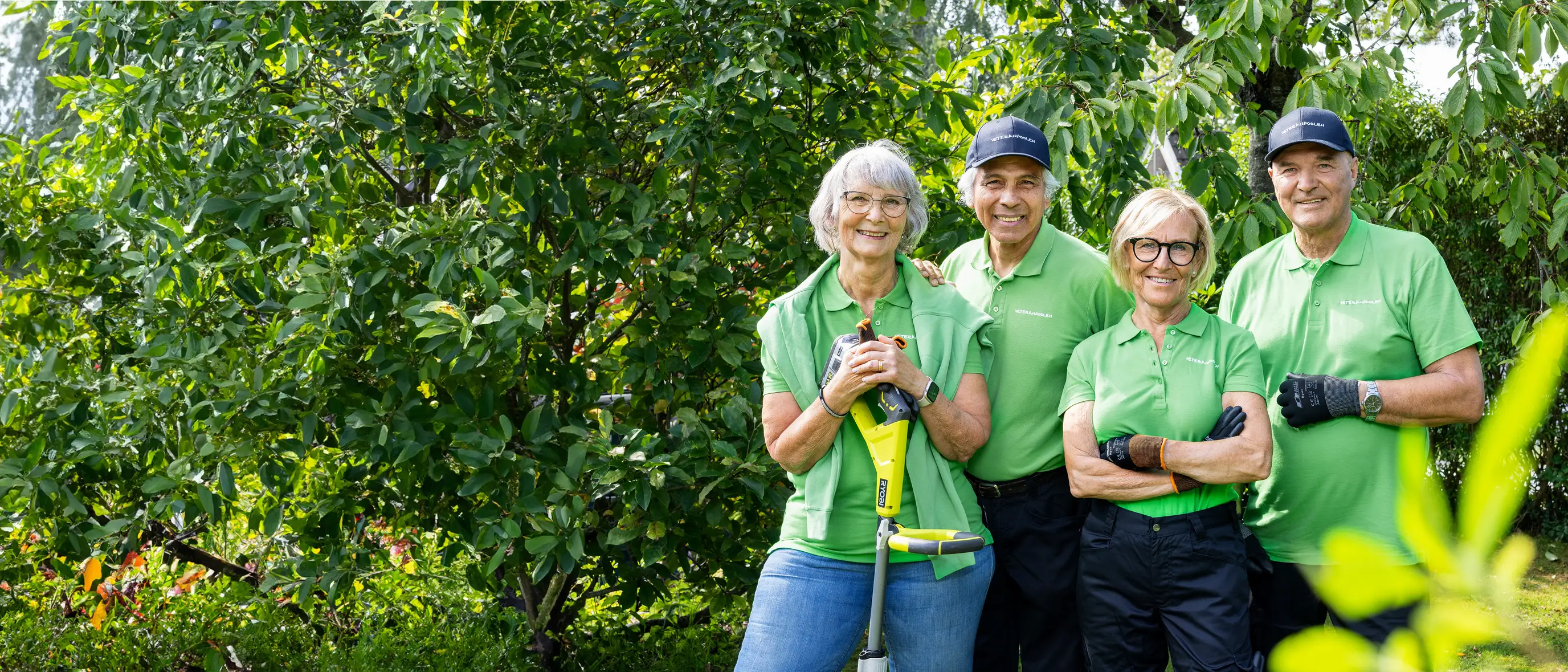 Fyra veteraner står bredvid varandra i en trädgård, de tittar mot kameran och ler