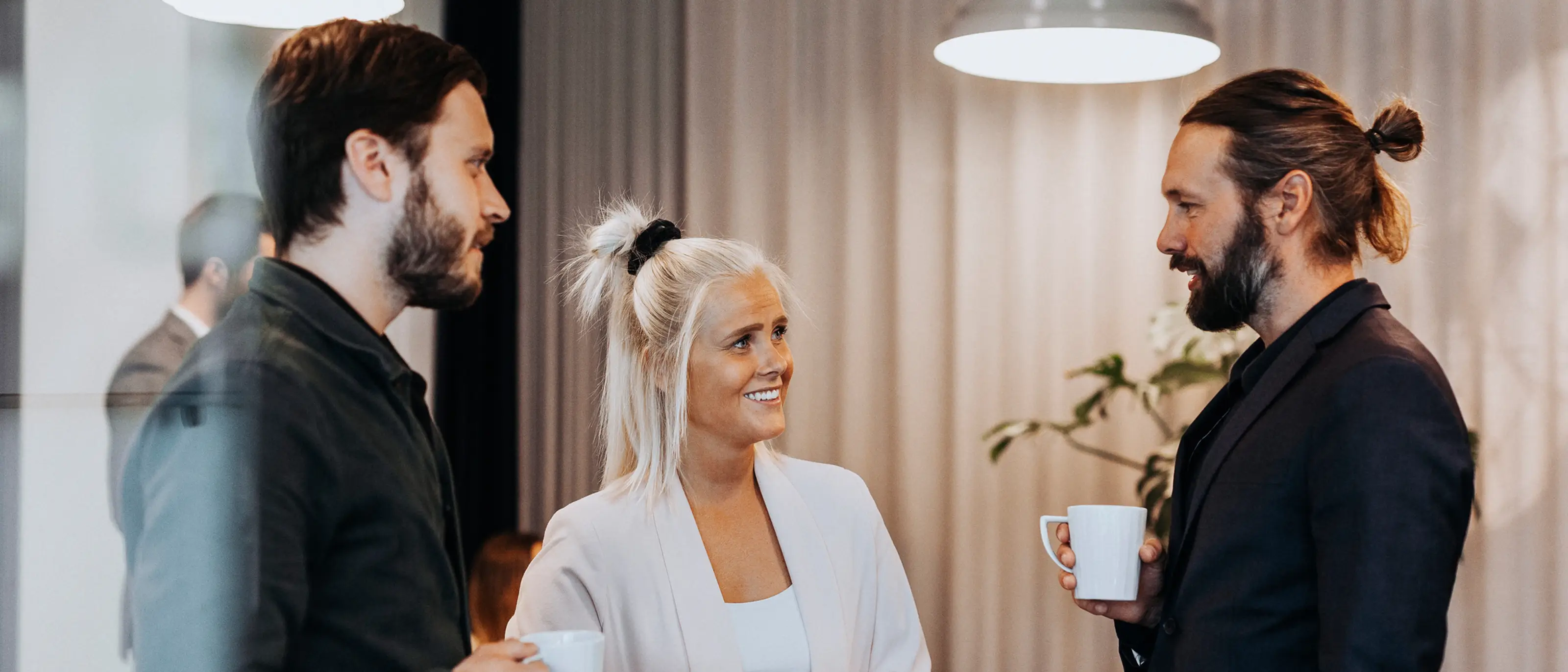 Tre kollegor står med varsin kopp i handen och pratar med varandra