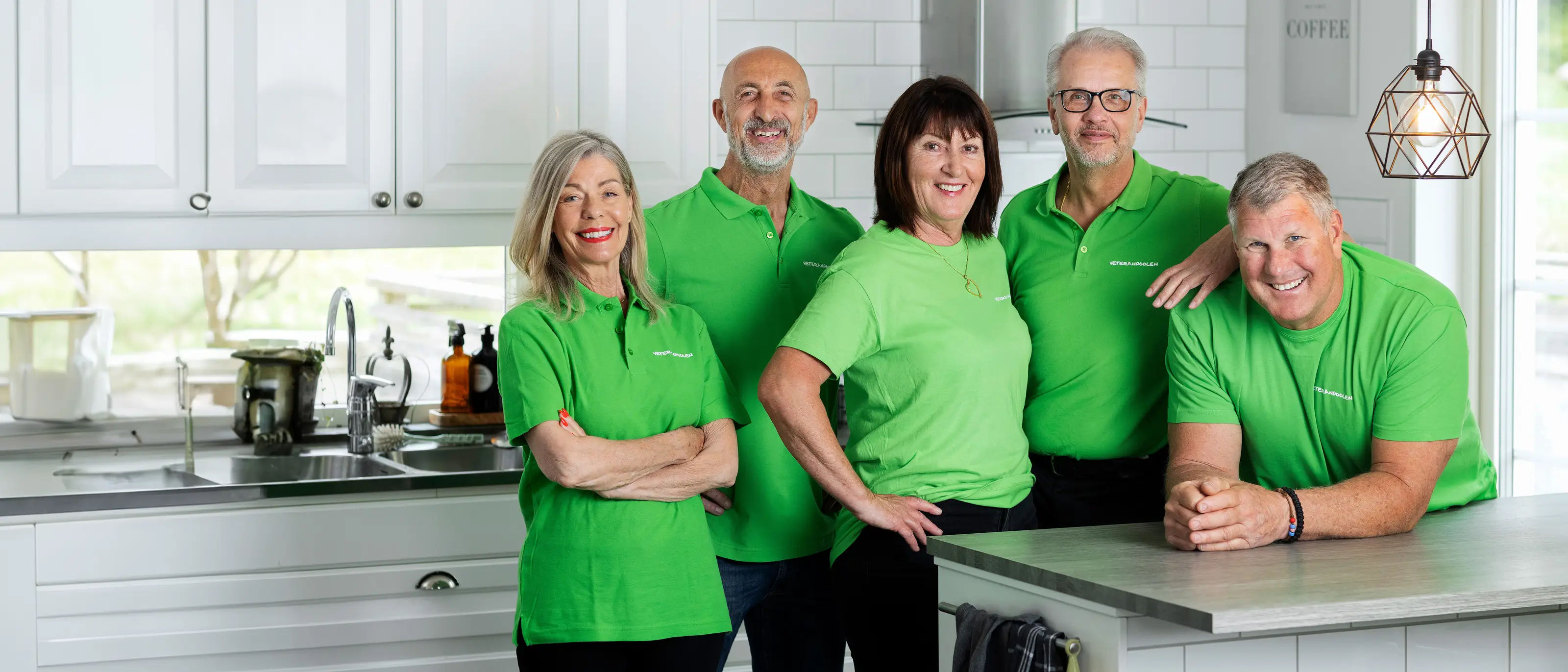 Fem veteraner i gröna tröjor står i ett kök, de tittar mot kameran och ler