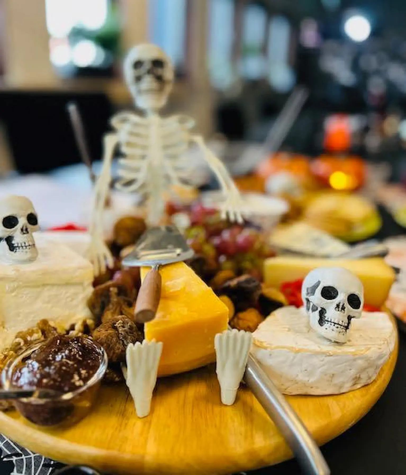 A Halloween-themed cheese board with assorted cheeses, grapes, figs, and small skeleton decorations on a wooden platter.