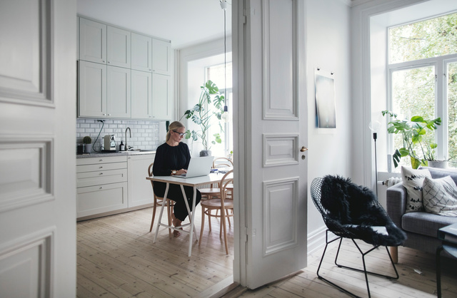 En kvinna jobbar med sin laptop i ett kök En kvinna jobbar med sin laptop i ett kök