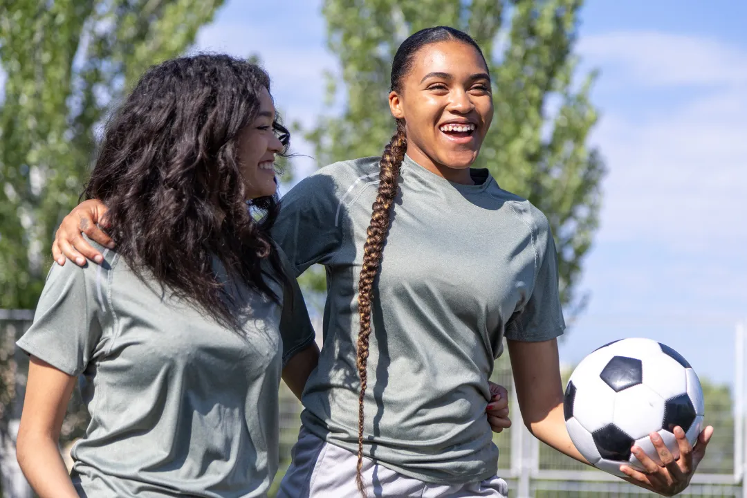 Zwei Frauen lächeln am outdoor Fußballplatz mit einem Ball in der Hand