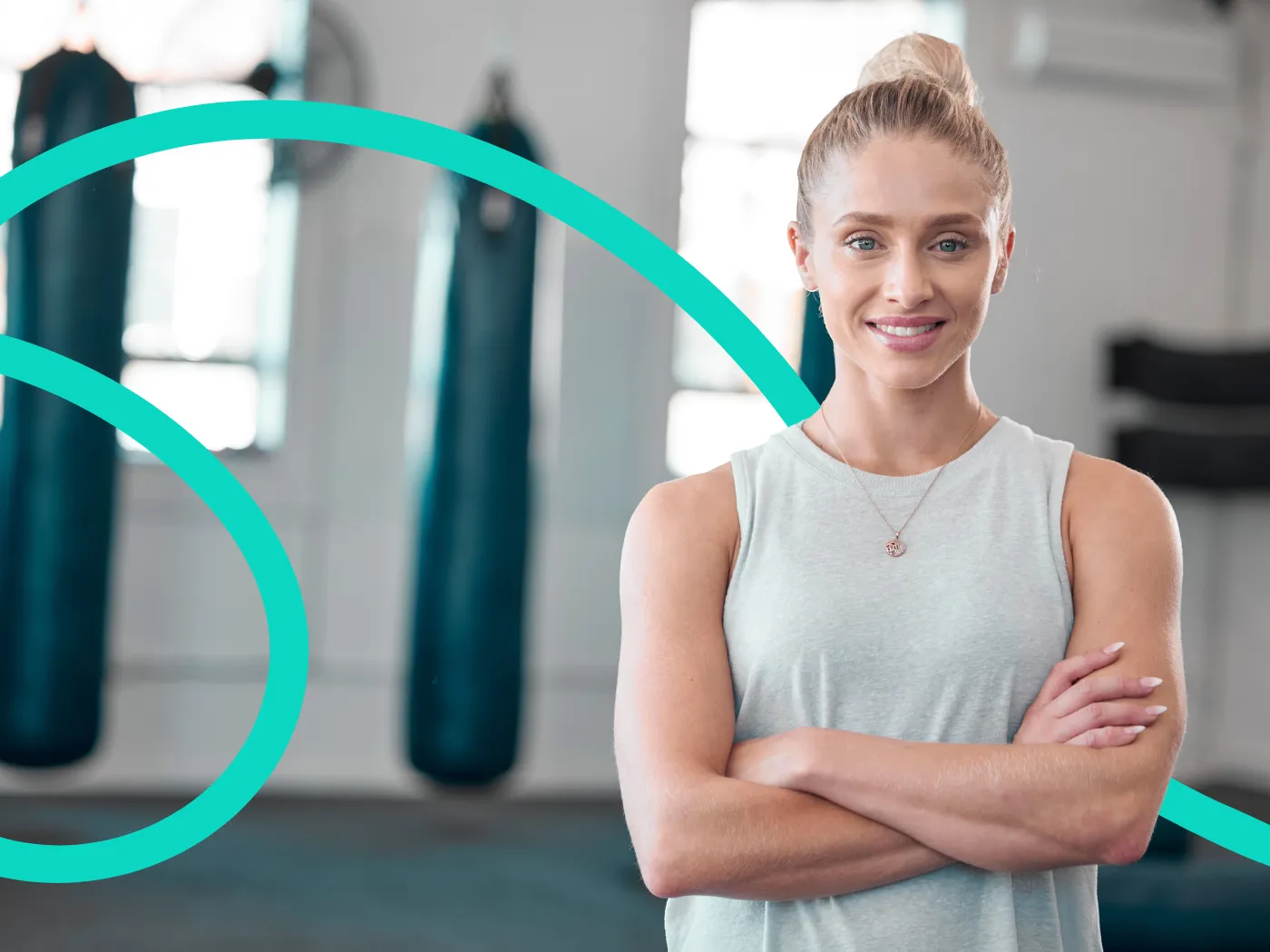 Frau in einem Fitnessstudio mit verschränkten Armen, trägt ein weißes Tanktop.