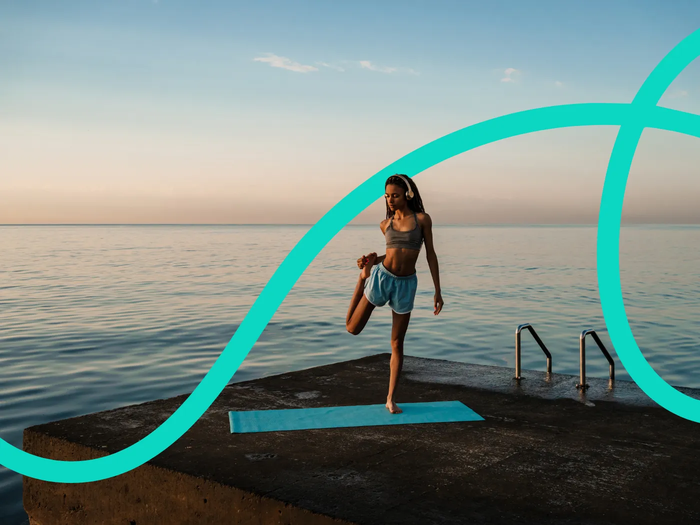 Eine Person dehnt sich bei Sonnenaufgang am Meer auf einer Yogamatte und trägt Sportkleidung.