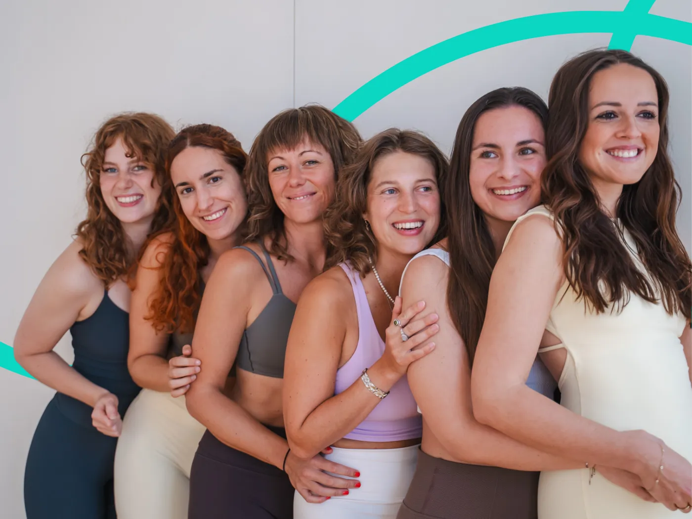 Sechs Frauen in Sportkleidung stehen in einer Reihe, lächeln und umarmen sich vor einem hellen Hintergrund.n in athletic wear stand in a line, smiling and embracing each other against a light background.